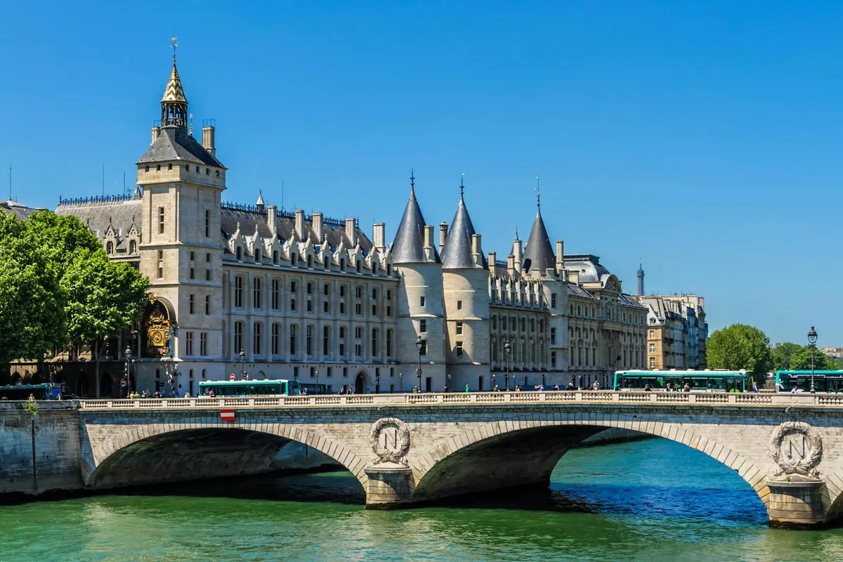 Bâtiment historique orné de tours coniques et pont enjambant une rivière, sous un ciel bleu clair.