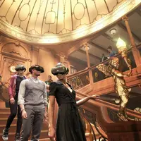 Des personnes portant des casques de RV dans une pièce ornée d'un grand escalier et d'un éclairage décoratif. &copy; TITANIC