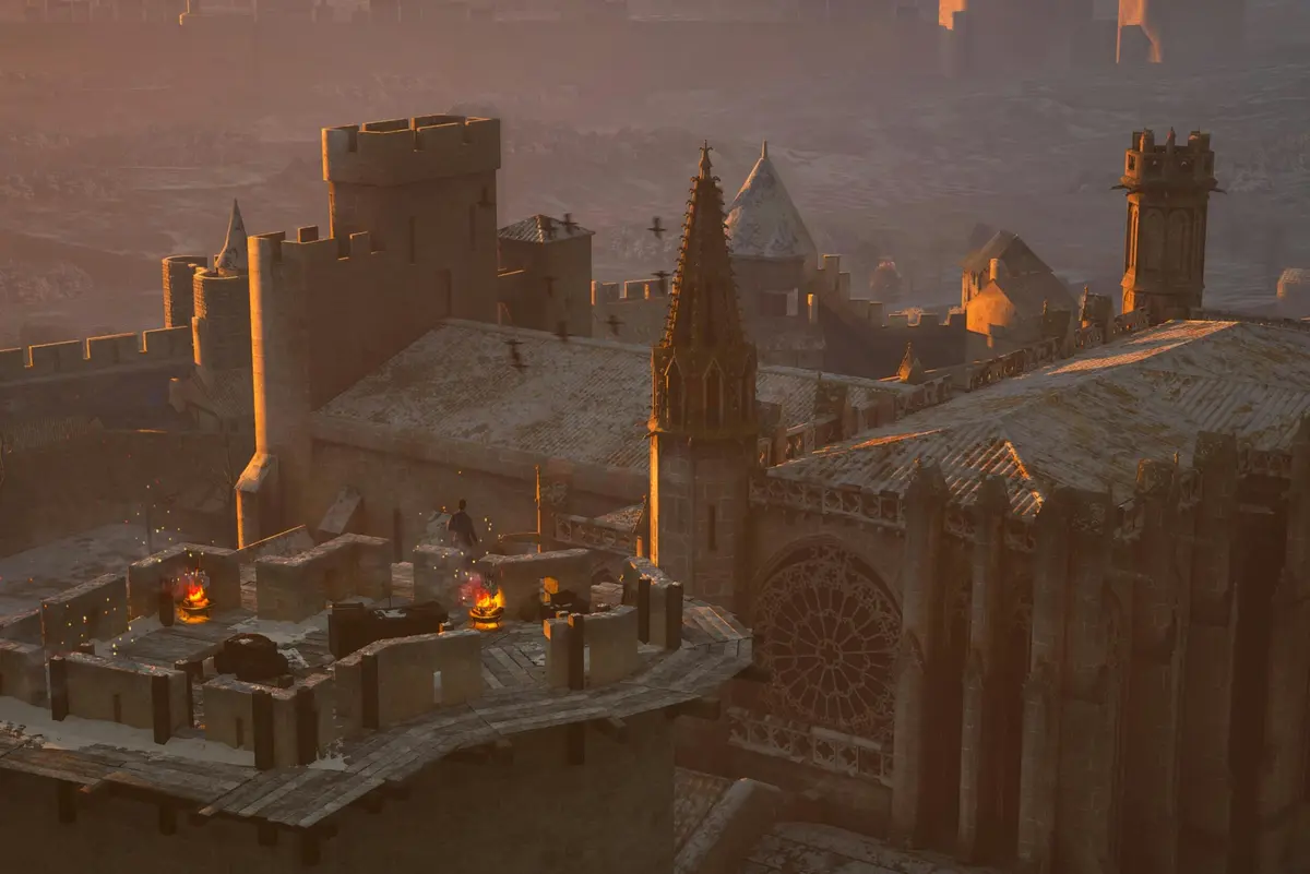 Toits d'un château médiéval au coucher du soleil avec un groupe de personnes autour d'un petit feu. L'architecture gothique et les flèches sont visibles.