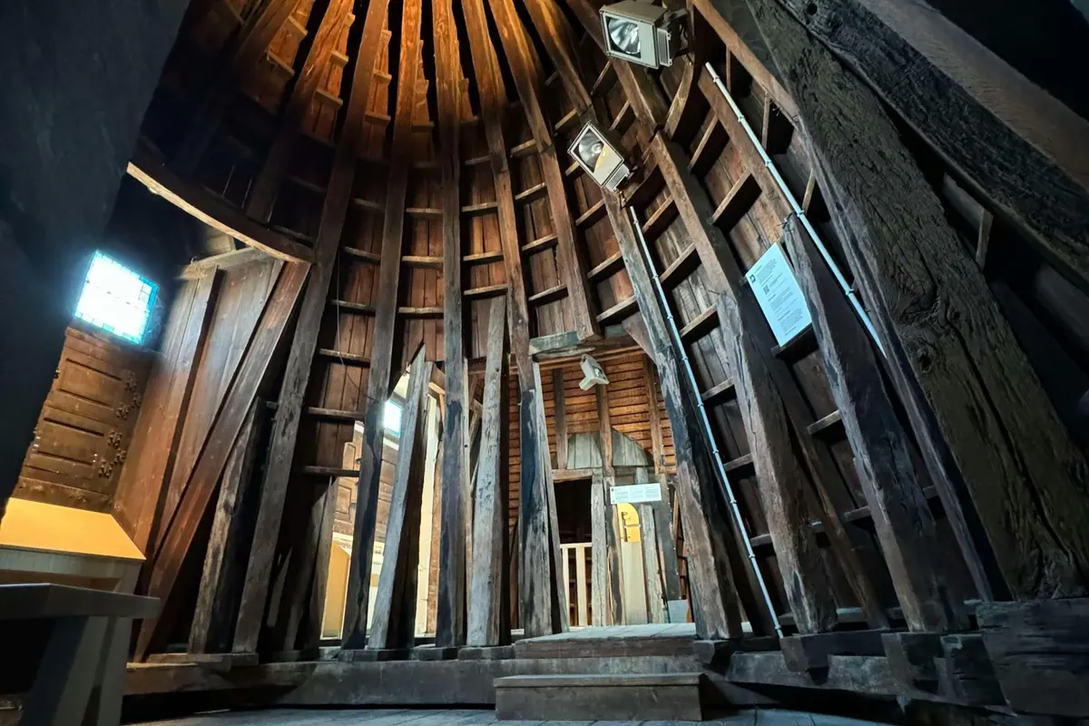 Intérieur d'une construction en bois avec de hautes poutres, un plafond voûté et des luminaires qui éclairent l'espace.