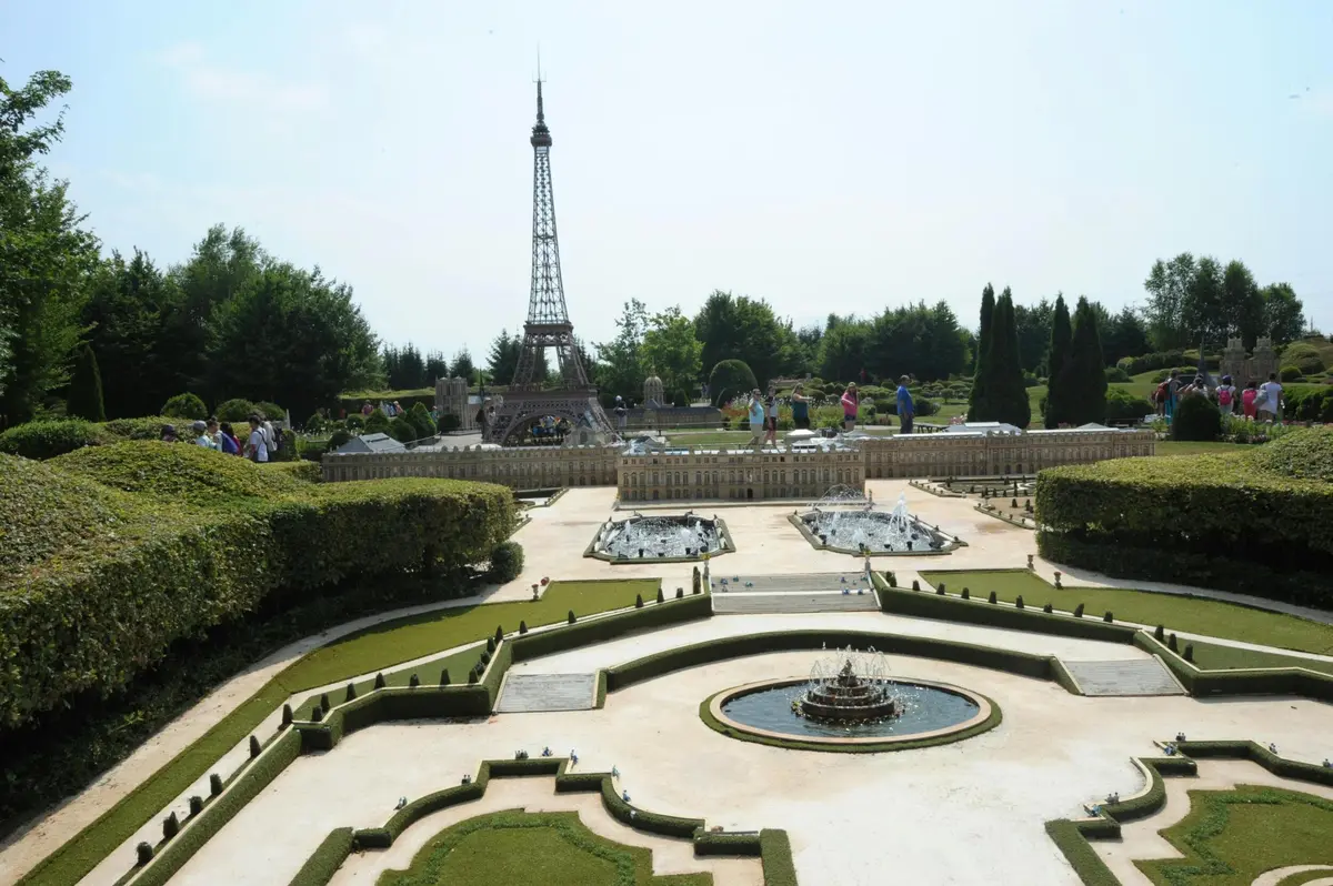 Un modèle réduit de la Tour Eiffel dans un jardin entretenu avec des allées, des fontaines et des bâtiments miniatures, entouré de verdure et de touristes.