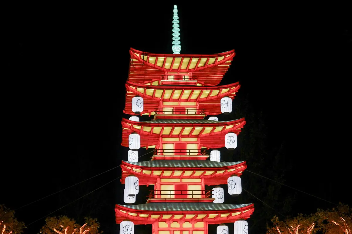 Une pagode rouge et jaune à plusieurs niveaux, brillamment éclairée, avec des lanternes suspendues la nuit.