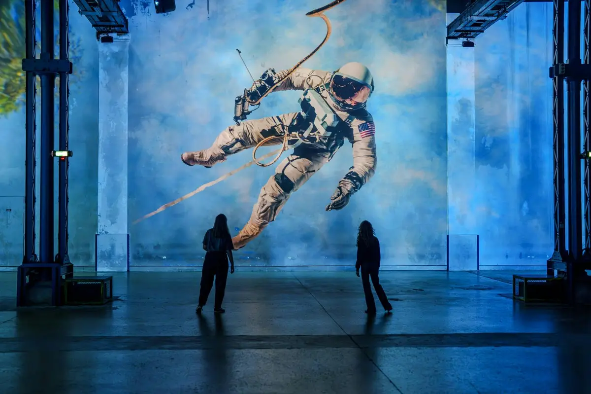 Deux personnes se tiennent devant une grande peinture murale représentant un astronaute flottant dans l'espace sur un mur aux tons bleus.