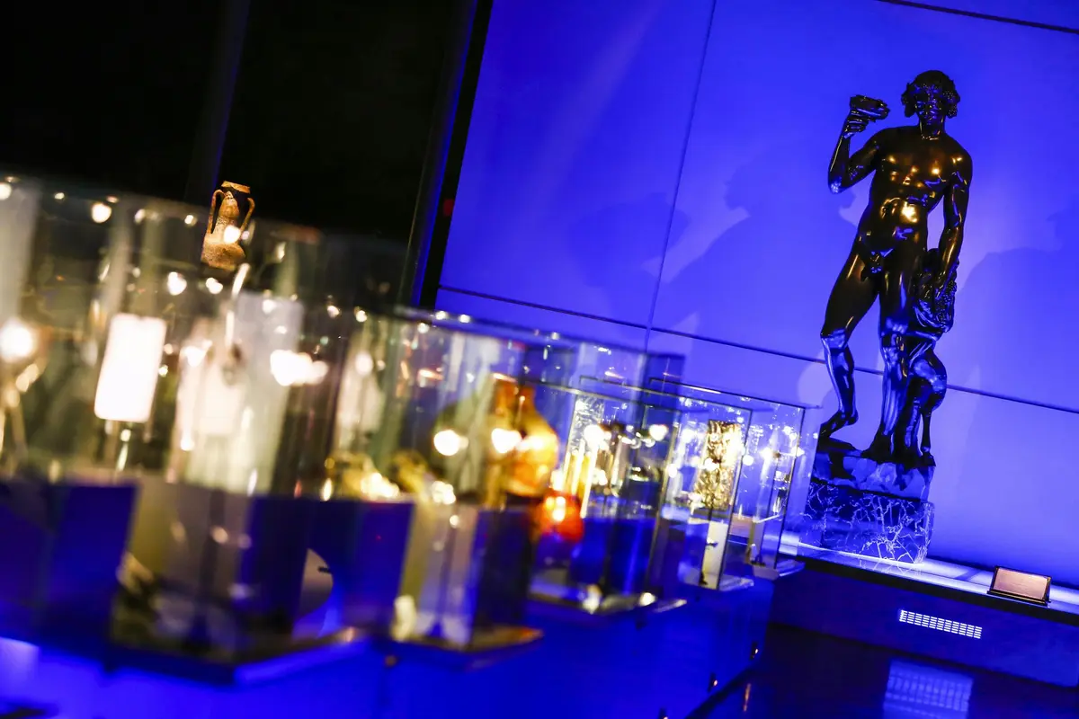 Vitrines avec divers objets illuminés ; une statue d'une personne tenant un objet se trouve à l'arrière-plan sur un mur éclairé en bleu.