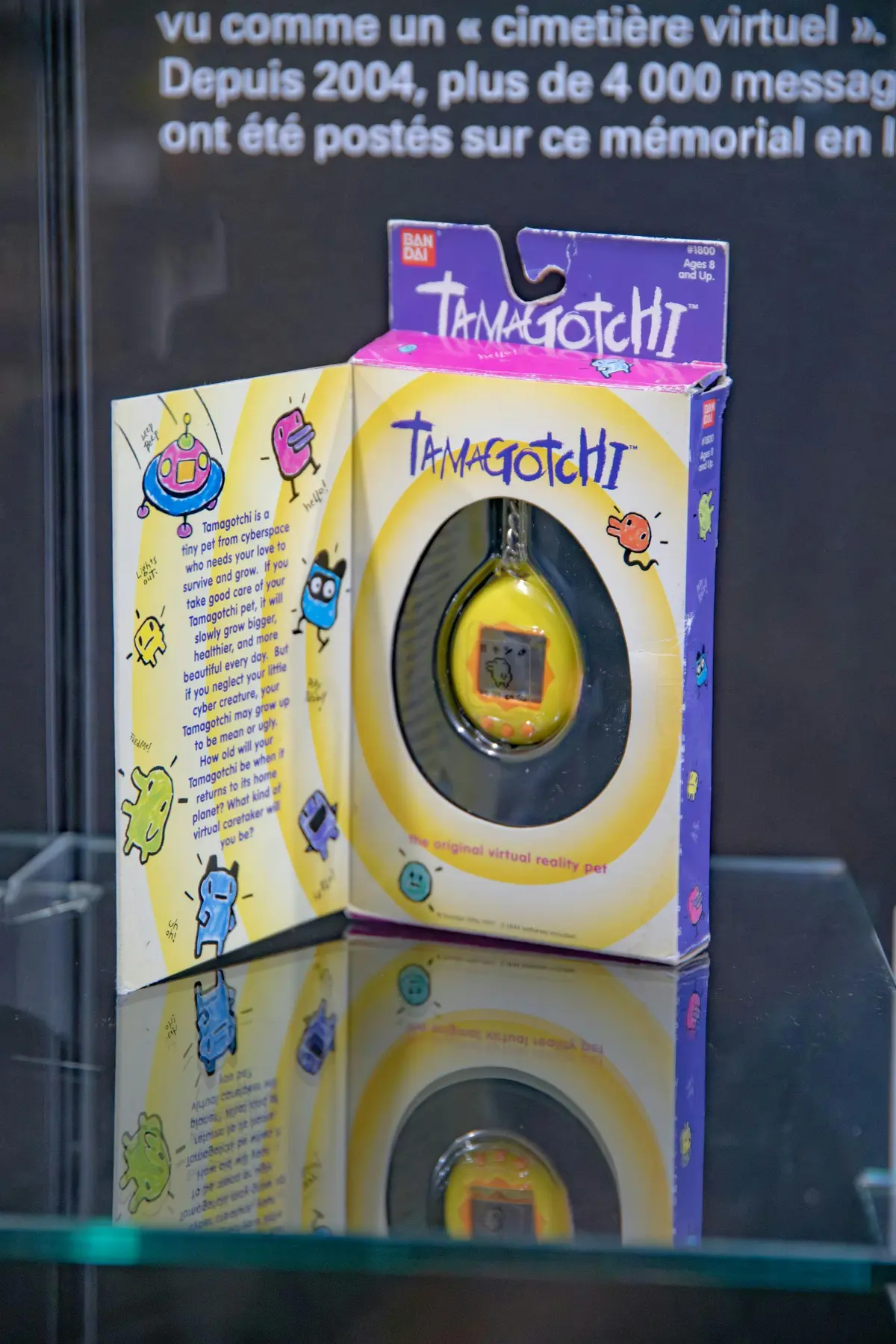 Une boîte de Tamagotchi, avec des illustrations de personnages colorés et la phrase The original virtual reality pet (l'animal de compagnie original de la réalité virtuelle), est présentée.