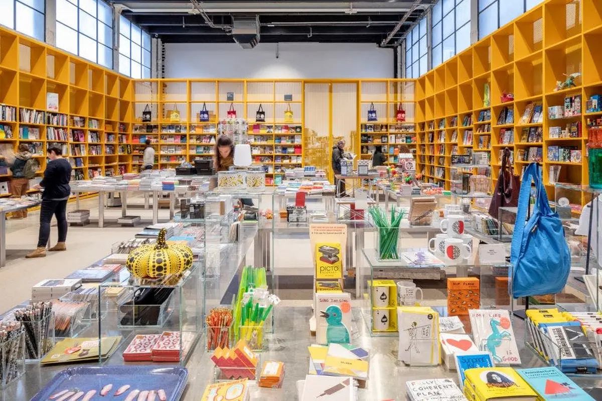 Un magasin bien éclairé, avec des étagères de livres et d'articles colorés, des clients qui naviguent et des produits exposés sur des tables.