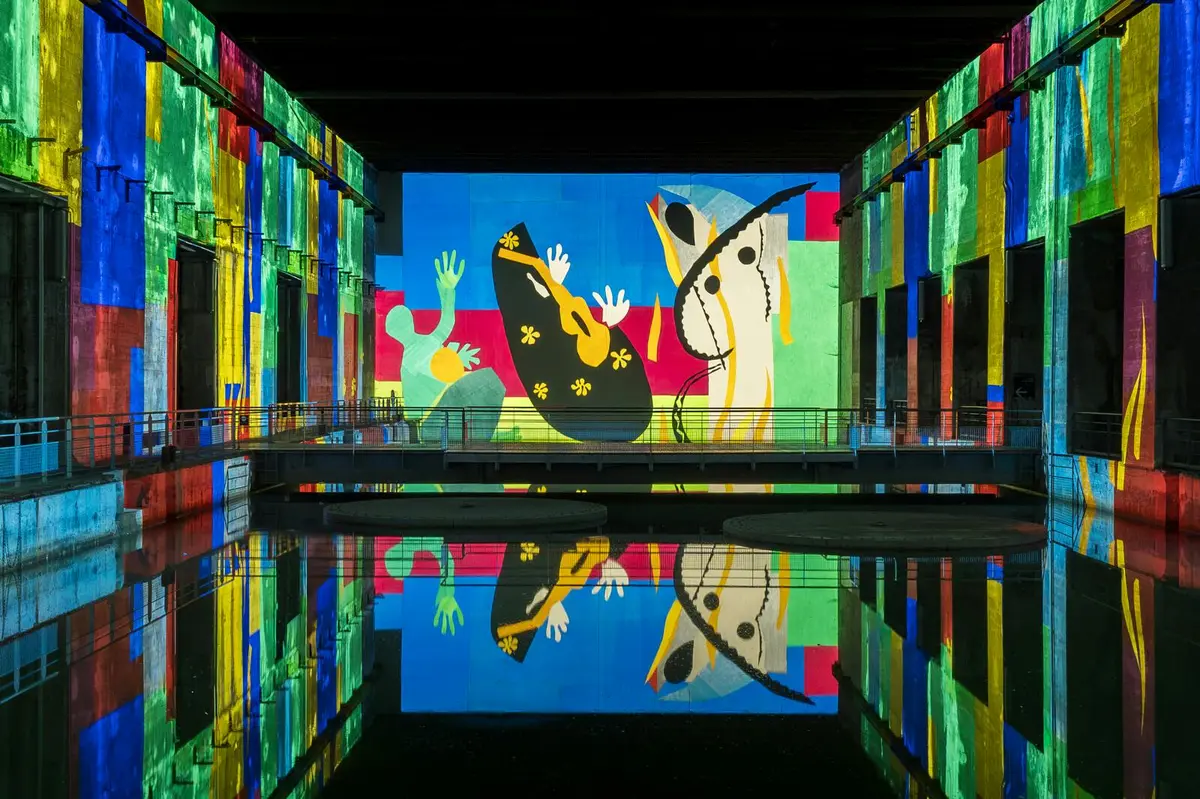 Une peinture murale vibrante avec des figures abstraites, des formes colorées et des reflets sur l'eau dans un espace de galerie.
