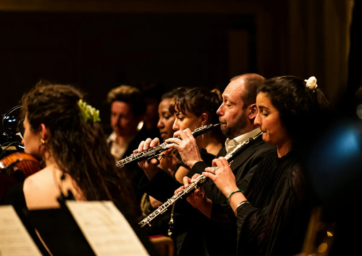 Des musiciens assis en rang, jouant du hautbois lors d'un concert, avec un gros plan sur ceux qui se trouvent au premier plan.