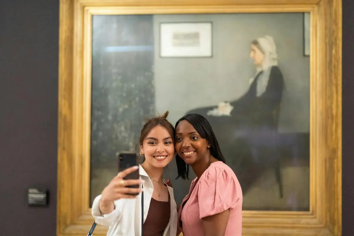Two guests taking a selfie in front of the painting of Whistler's mother
