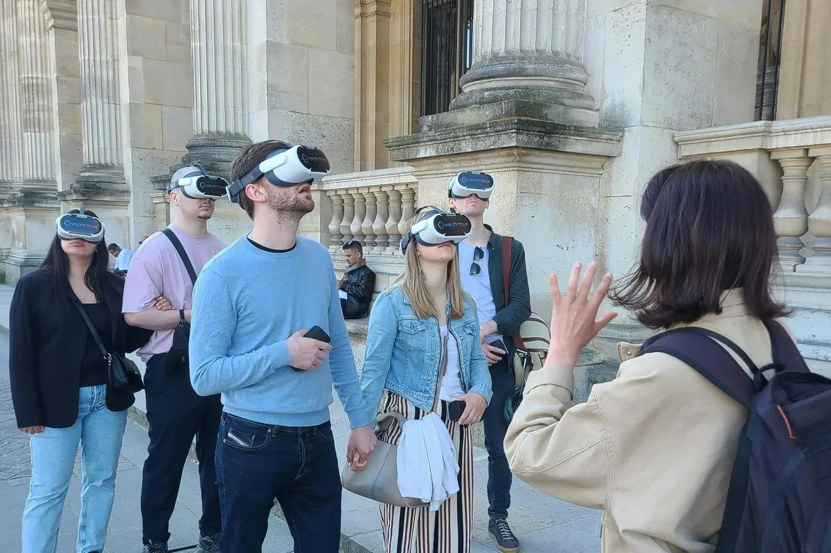 Un groupe de personnes portant des casques de RV en plein air, près d'un bâtiment classique avec des colonnes en pierre.