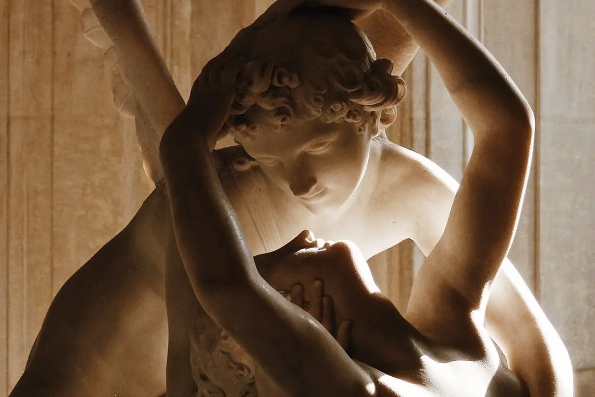 Gros plan d'une sculpture en marbre représentant deux personnages entrelacés, l'un tenant délicatement la tête de l'autre, avec des expressions de tendresse.