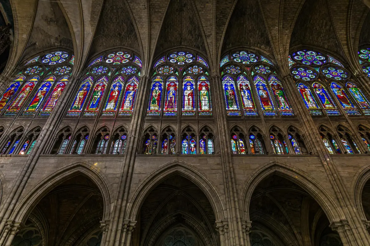 Vitraux colorés représentant diverses scènes et saints dans une grande cathédrale à l'intérieur voûté.