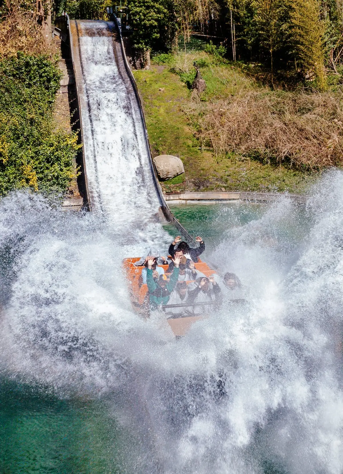 Un groupe de personnes sur un toboggan à billes s'éclaboussant dans l'eau avec de grands jets, entouré de verdure.