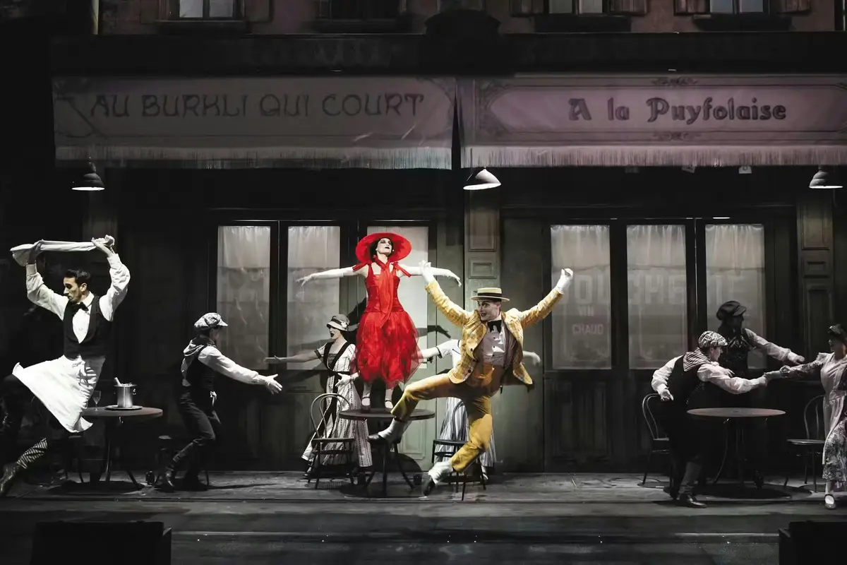 Un spectacle mettant en scène des danseurs vêtus de costumes colorés sur une scène reproduisant l'ambiance d'un café parisien.