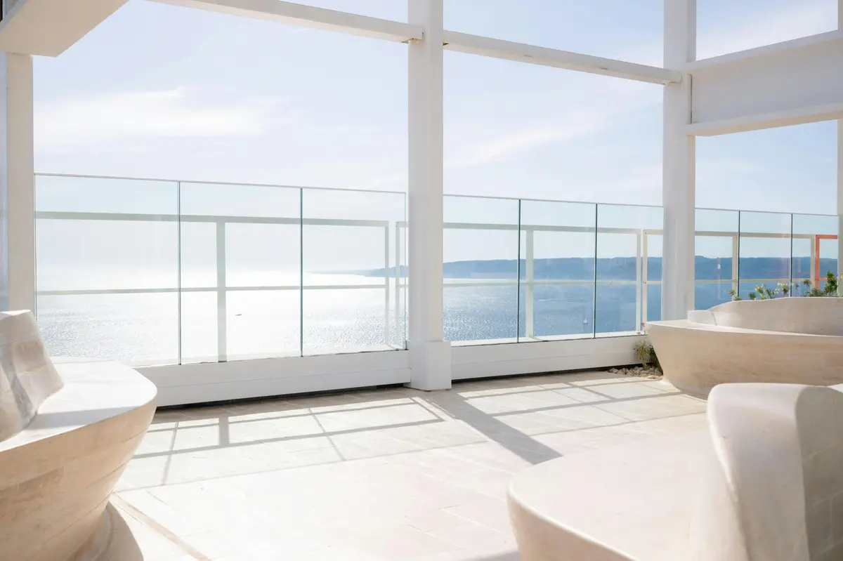 Une terrasse spacieuse et moderne, dotée de garde-corps en verre, donne sur un plan d'eau serein et un littoral lointain sous un ciel dégagé.