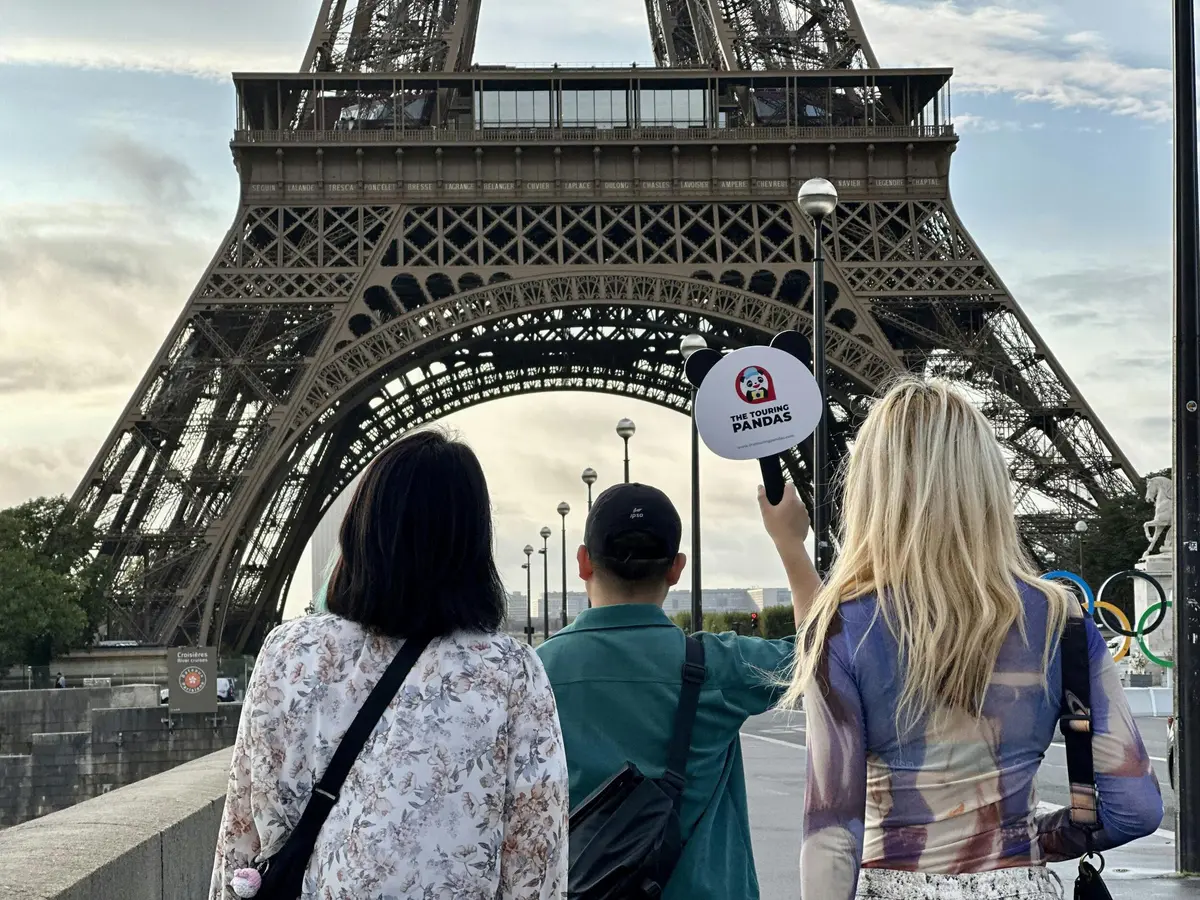Trois personnes face à la Tour Eiffel ; l'une d'elles tient un signe de panda.