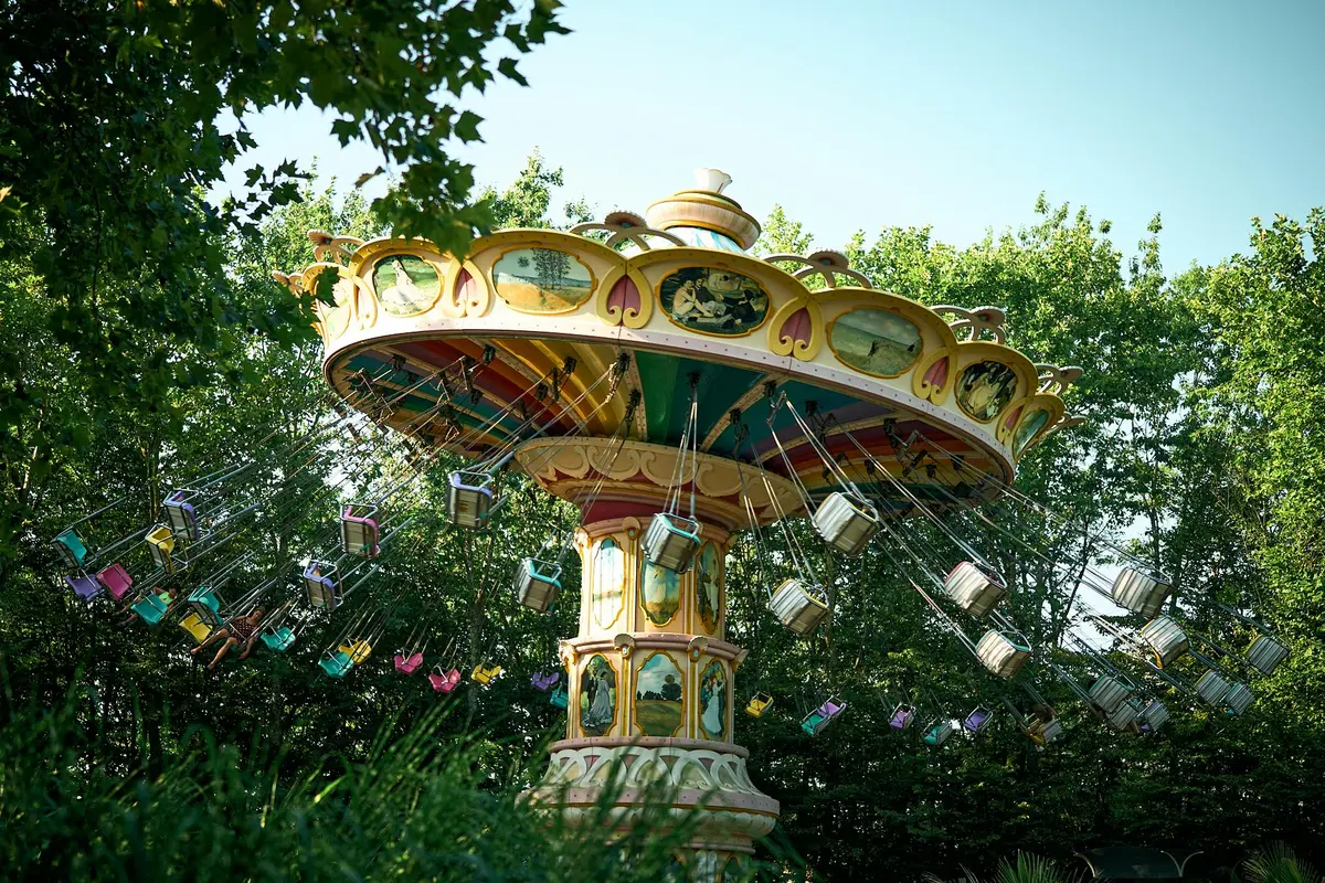 Un manège de balançoires vintage et coloré dans un parc d'attractions, avec des balançoires vides suspendues, entourées d'arbres et de verdure.