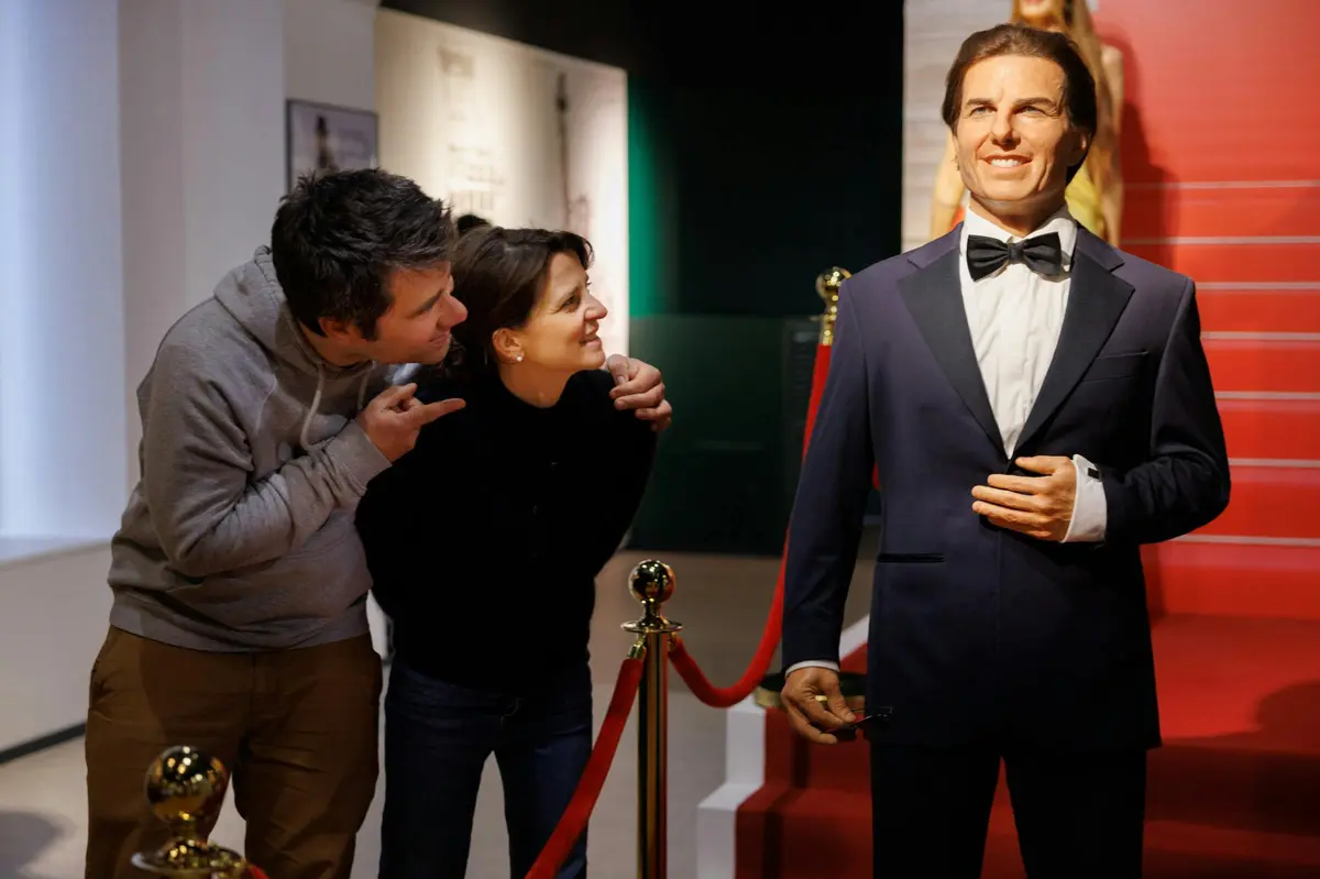 Deux personnes admirent une statue de cire représentant un homme en costume et nœud papillon, exposée dans un musée.
