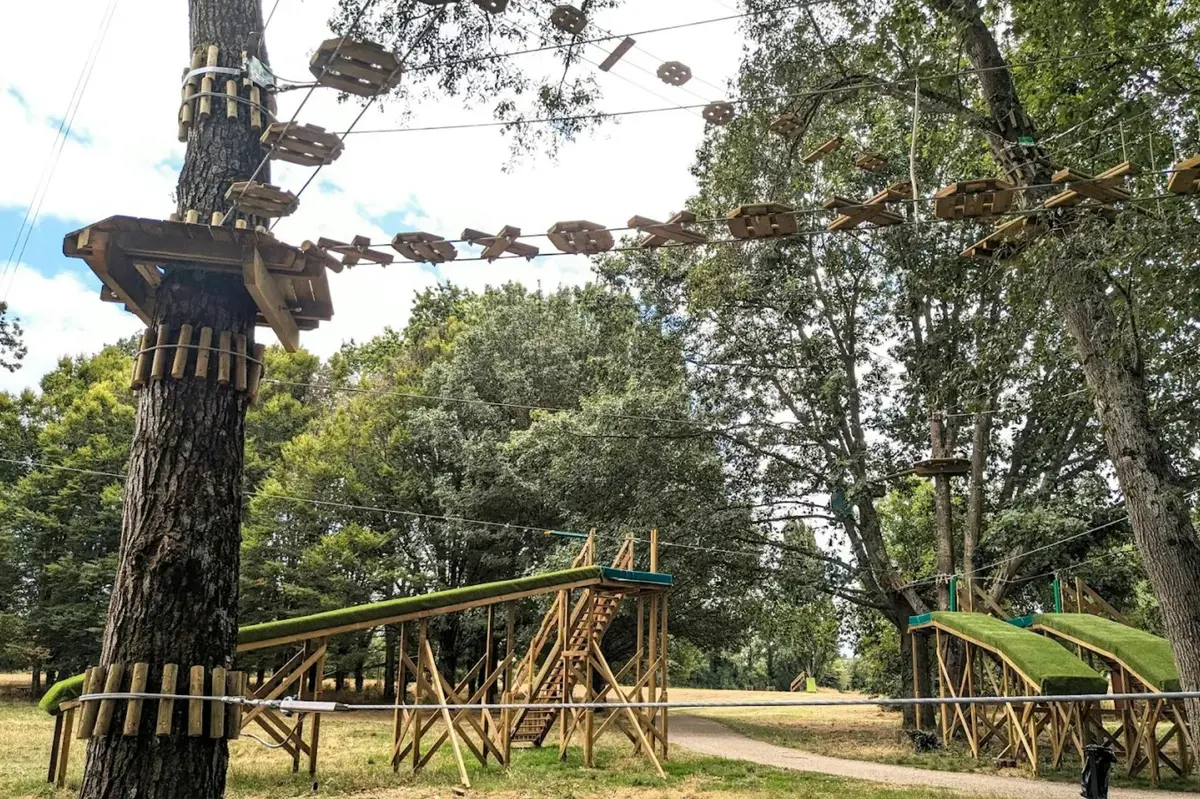 Parcours de cordes en plein air avec des plates-formes et des ponts en bois au milieu de grands arbres dans un parc.