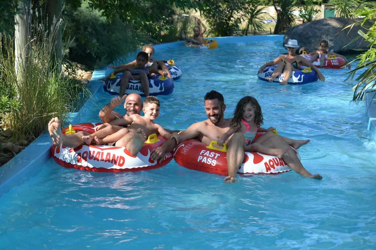 Des personnes profitant de l'attraction lazy river d'un parc aquatique, flottant dans des chambres à air de marque portant l'inscription Aqualand.