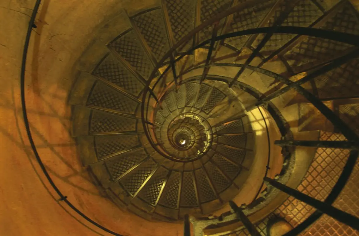 Un escalier en colimaçon avec des marches et des rampes en métal, vu d'en haut, créant un motif circulaire menant vers le bas.