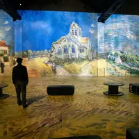 Une personne se tient dans une pièce où sont projetées des œuvres de Van Gogh représentant une église et un paysage, entourée de sièges. &copy; Culturespaces___Cyrille_de_la_Motte_Rouge