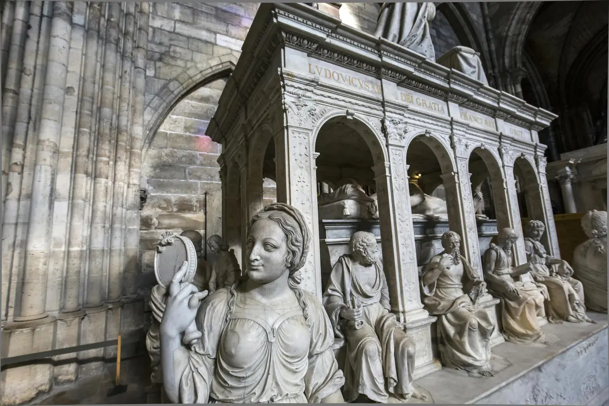 D'élégantes statues de marbre, dont une femme avec un miroir, se dressent sous une structure voûtée ornée, à l'intérieur d'un bâtiment aux murs de pierre.