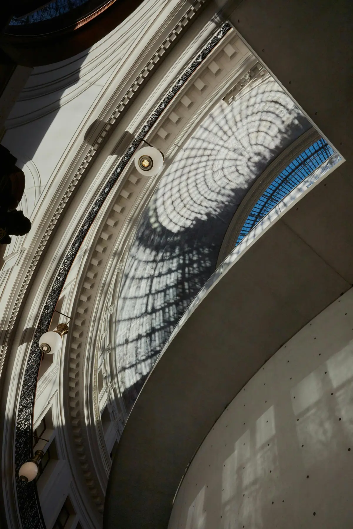 La lumière du soleil crée des ombres complexes sur un plafond courbé et orné, doté d'une grande fenêtre cintrée.