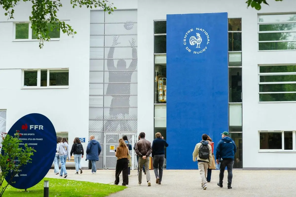 Des personnes se dirigeant vers un bâtiment à la façade bleue portant l'inscription « Centre National de Rugby ».
