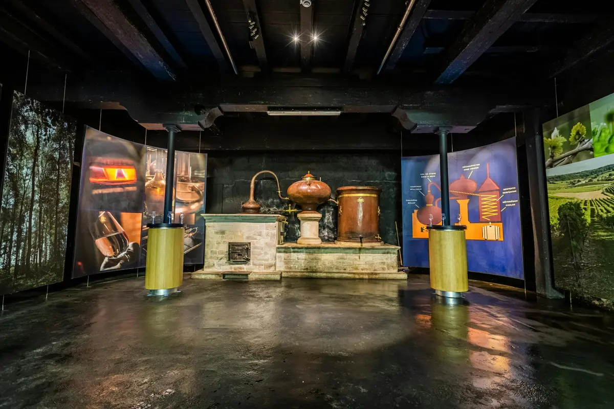 Exposition de matériel de distillation en cuivre entouré de panneaux d'information dans une pièce faiblement éclairée.