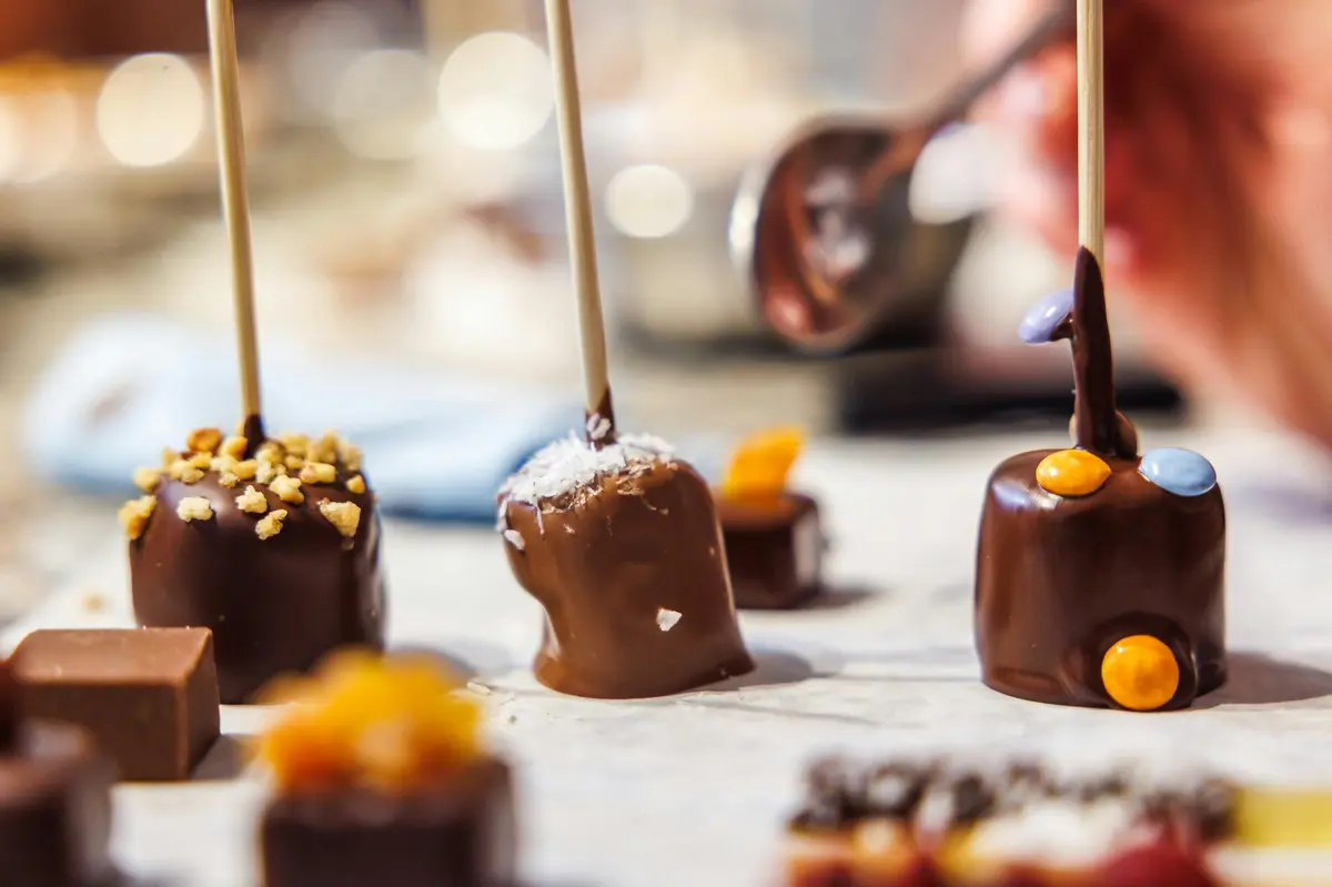 Friandises enrobées de chocolat sur des bâtonnets, décorées de noix, de noix de coco et de bonbons, avec un arrière-plan flou.