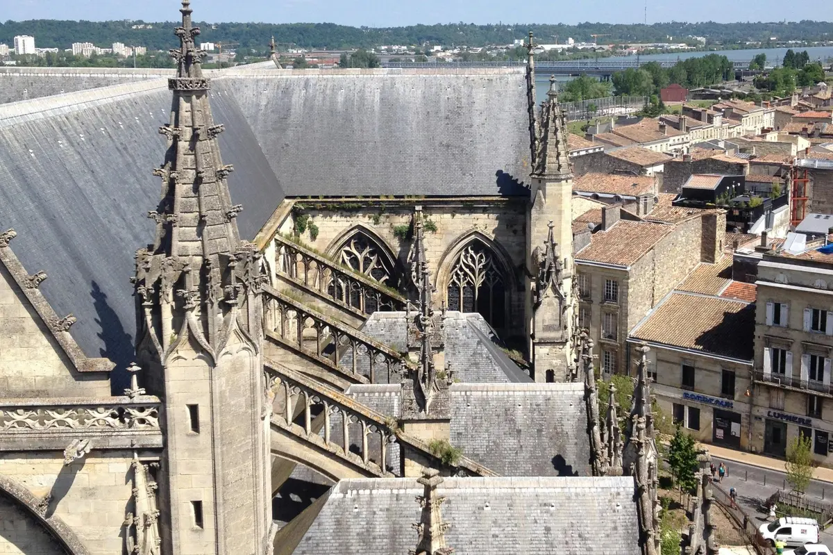 Vue aérienne d'une église gothique avec des arcs-boutants, des arcs brisés et des bâtiments environnants sous un ciel clair.