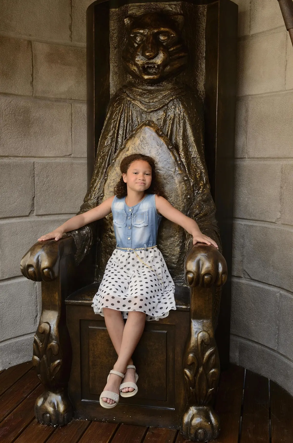 Une jeune fille vêtue d'un haut en jean et d'une jupe à pois est assise avec assurance sur un grand trône orné en forme de créature.