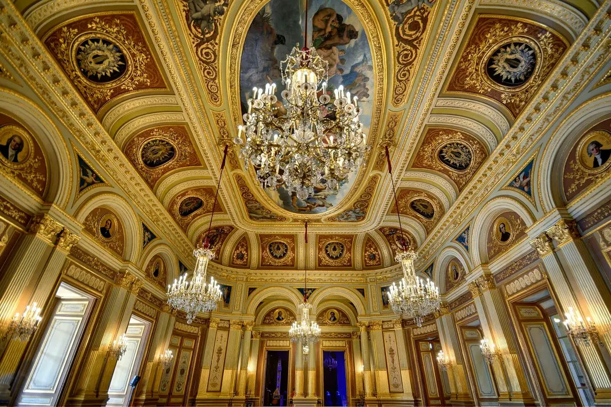 Une pièce somptueuse, richement décorée, avec des lustres, des fenêtres cintrées et un plafond peint dans un style classique.