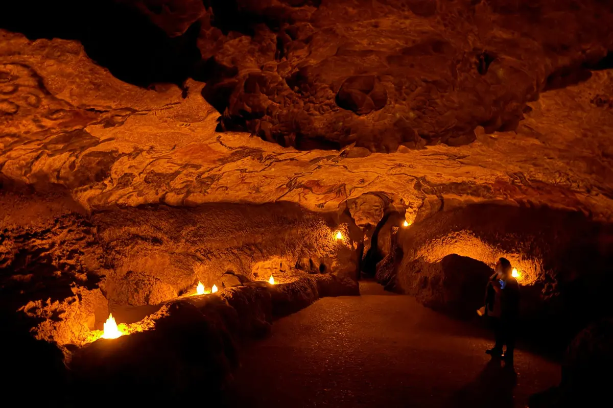 Intérieur d'une grotte faiblement éclairée, avec un chemin sinueux et éclairé par de petites lumières ; une personne se tient sur le côté droit pour observer.