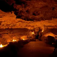 Intérieur d'une grotte faiblement éclairée, avec un chemin sinueux et éclairé par de petites lumières ; une personne se tient sur le côté droit pour observer. DR