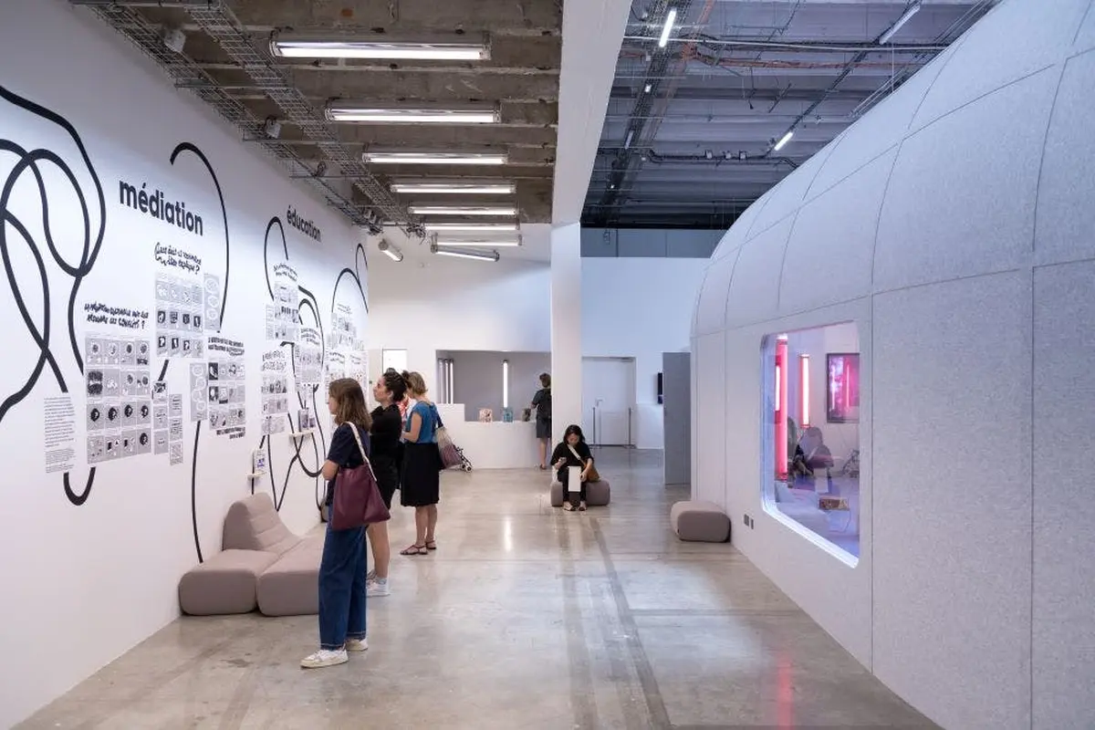 Un espace d'exposition moderne où les gens regardent les expositions murales et s'assoient sur un mobilier minimal, avec un éclairage lumineux.