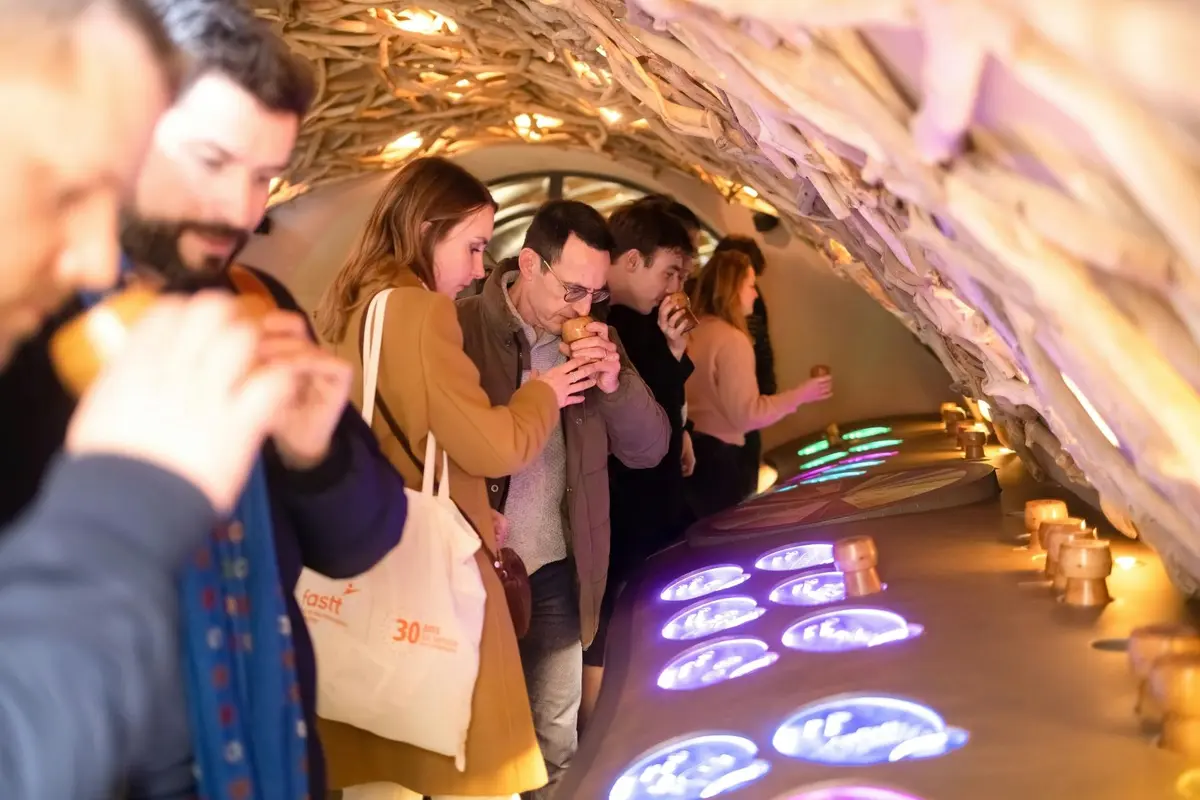 Des personnes se tenant en ligne sous une arche en bois, portant des objets à leur nez, s'adonnant peut-être à une activité sensorielle.