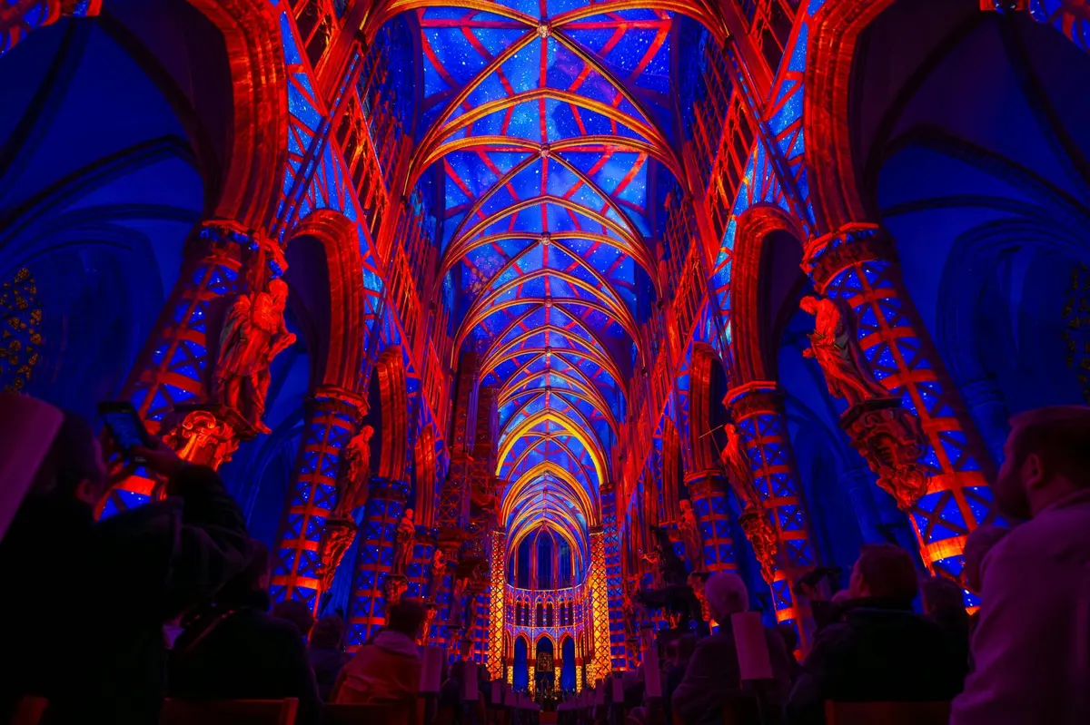 Intérieur d'une cathédrale baigné d'un éclairage bleu et rouge vif, mettant en valeur les arcades, les statues et les vitraux.