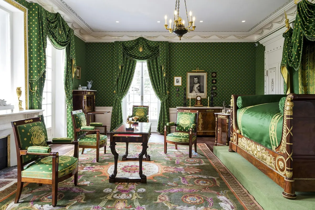 Une chambre luxueuse avec un papier peint et des rideaux verts, des meubles ornés, un lustre et un tapis décoratif.