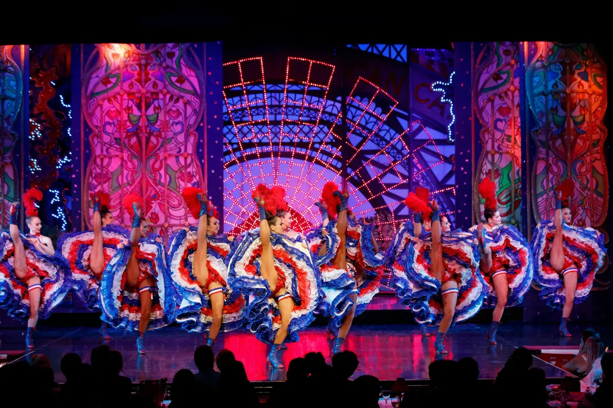 Des danseurs vêtus de costumes colorés se produisent sur une scène baignée d'un éclairage éclatant, devant un décor somptueux.