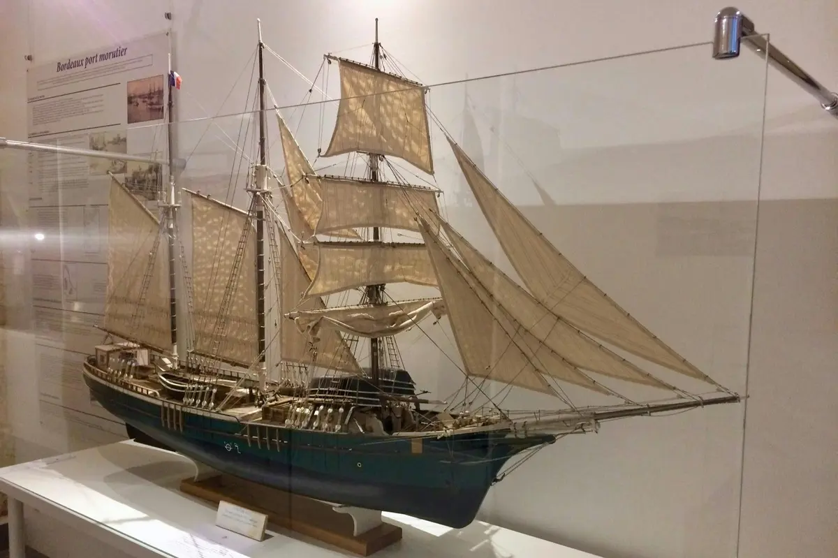 Modèle détaillé d'un voilier à plusieurs mâts et voiles, présenté dans un cadre muséal sur un socle blanc.