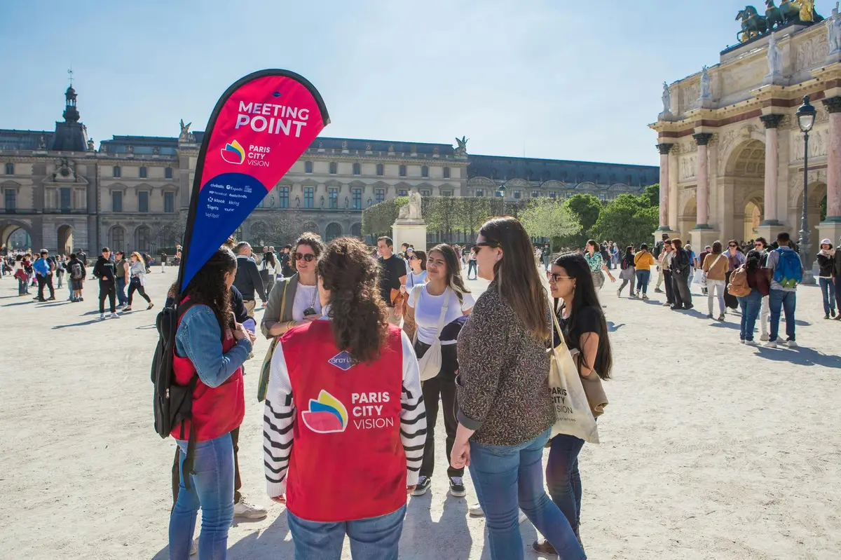 Un groupe de personnes se tenant près d'un panneau Meeting Point pour Paris City Vision sur une place ensoleillée avec des bâtiments historiques.