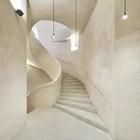 Un escalier minimaliste et incurvé dans un intérieur aux tons beiges, avec trois lampes suspendues au plafond. DR