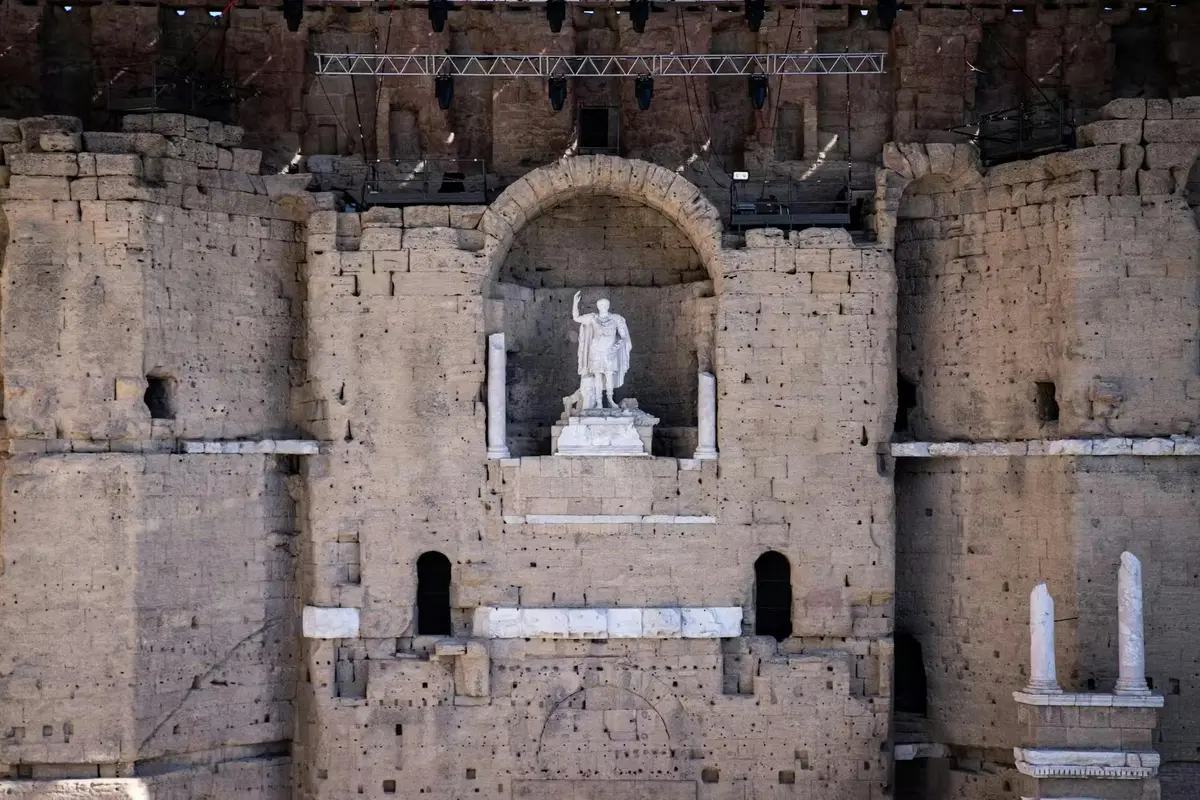 Mur de pierre avec statue d'un personnage vêtu dans une alcôve. De grandes ouvertures rectangulaires et des plafonniers sont visibles.