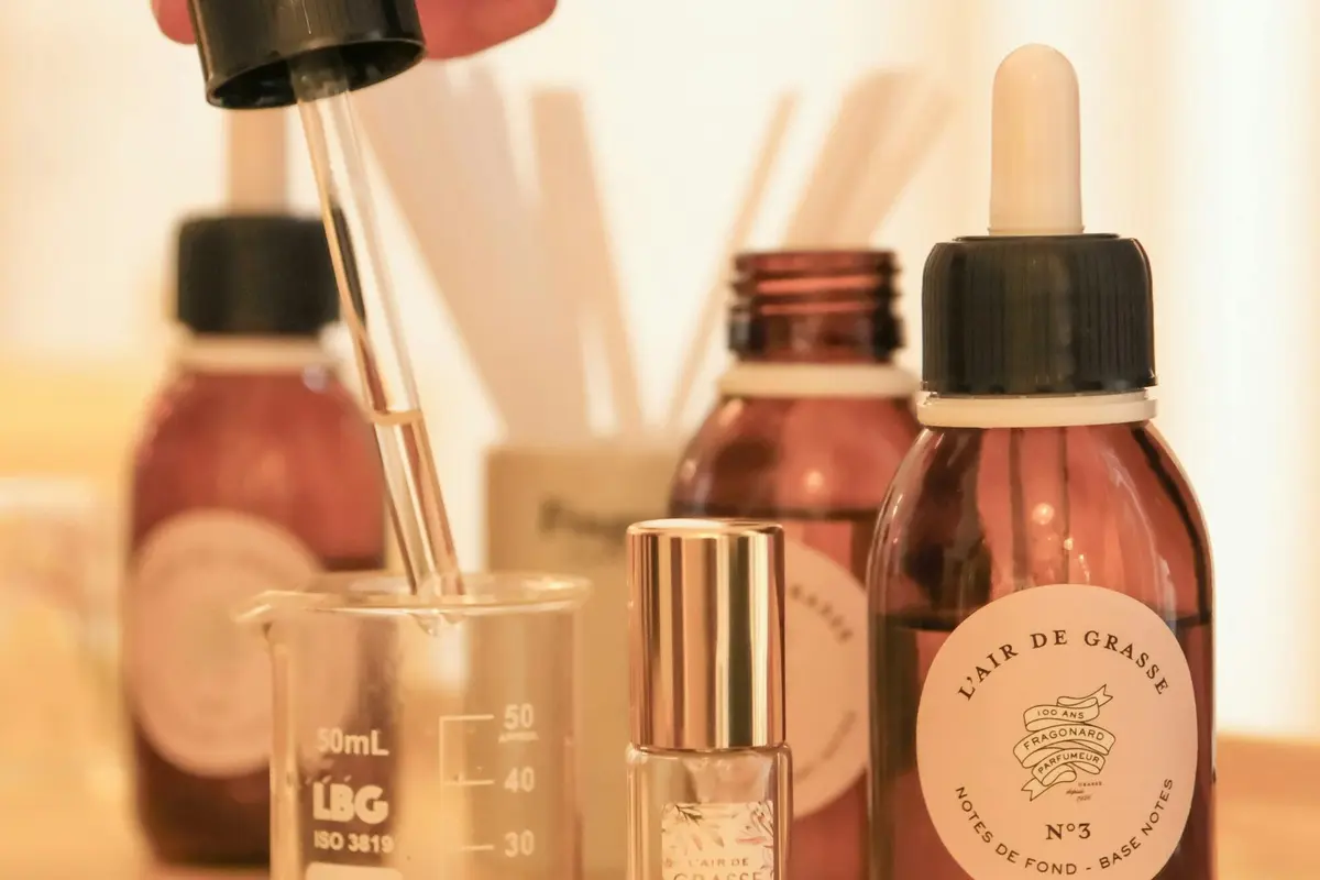 Gros plan sur des outils utilisés pour la fabrication de parfums, notamment des compte-gouttes, des béchers et des flacons étiquetés, disposés sur une surface.