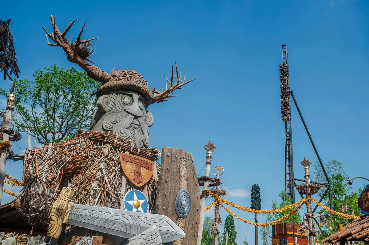 Une grande statue représentant un Viking, sculptée dans le bois et ornée de boucliers et de motifs, se détachant sur un ciel bleu limpide.
