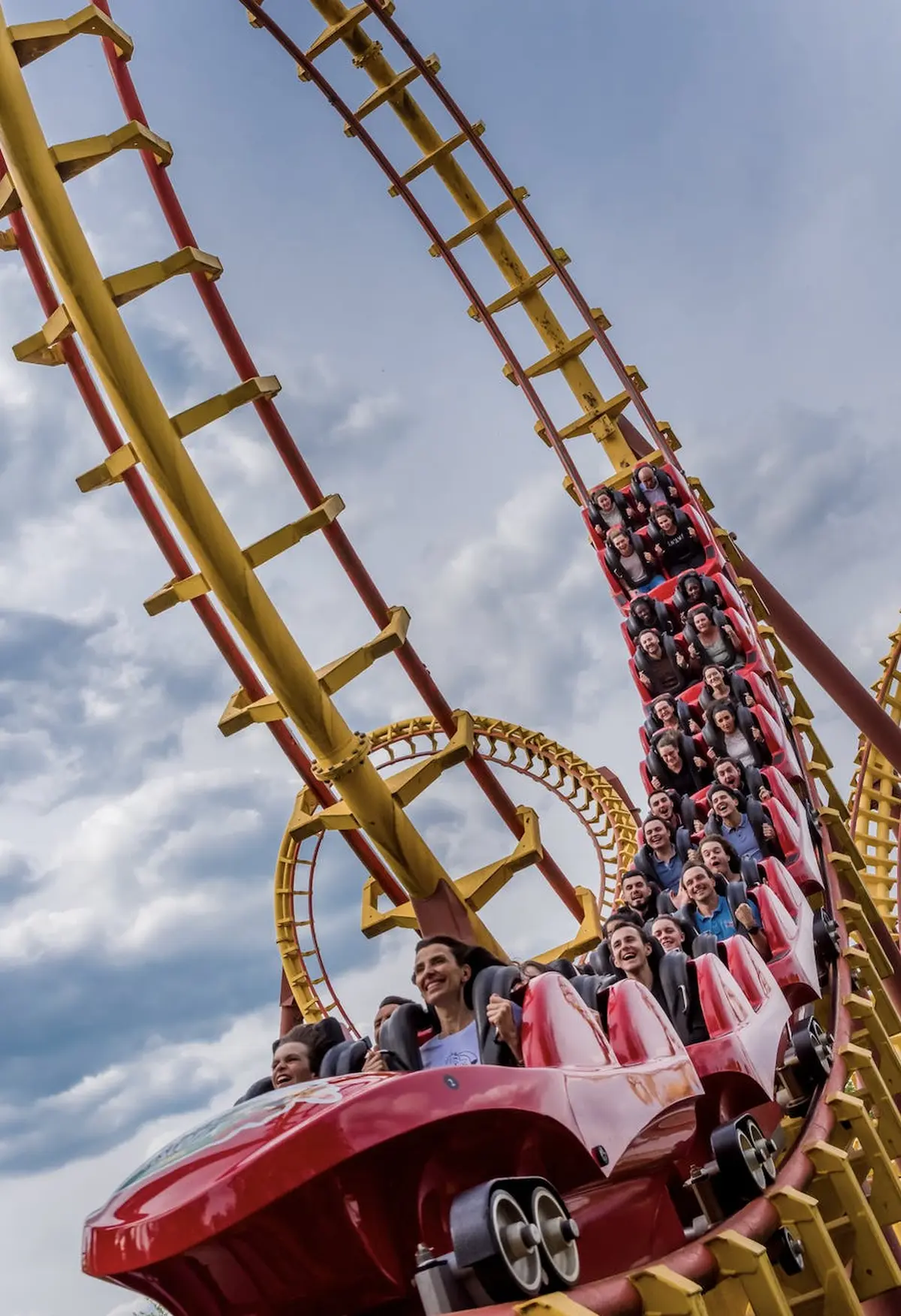 Des personnes montent sur des montagnes russes rouges avec un circuit en boucle, souriant et appréciant le trajet sous un ciel nuageux.