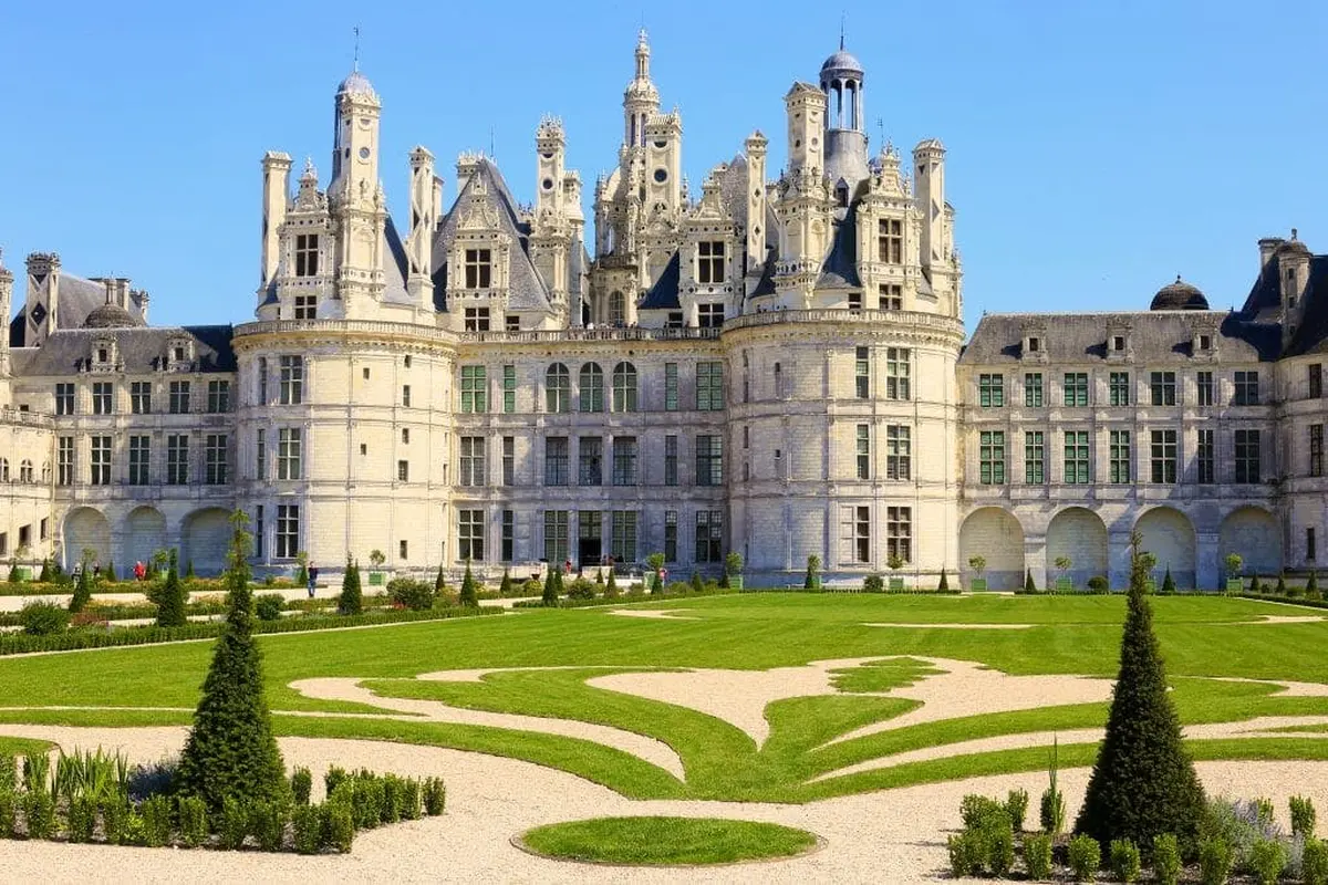 Grand château orné de tours et de flèches complexes, entouré de pelouses entretenues et d'allées de jardin décoratives.
