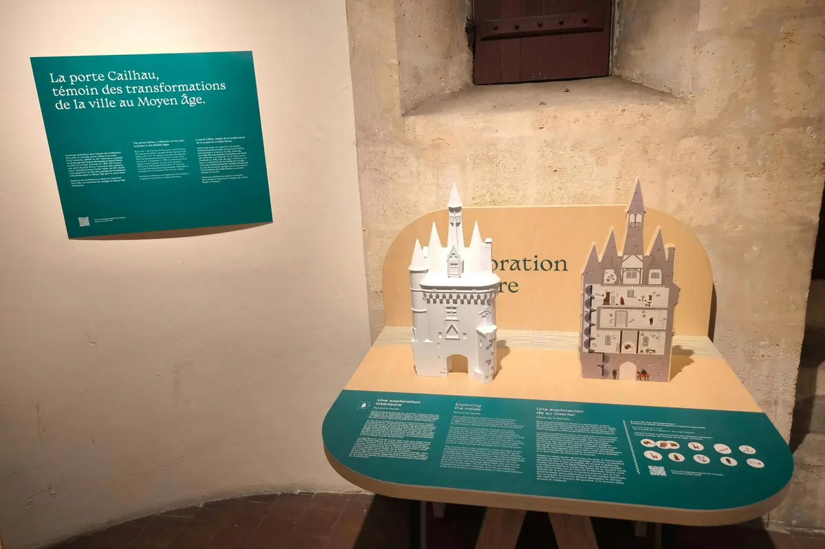 Display of two architectural models of medieval castles, accompanied by informational panels with text in French on a wooden table.